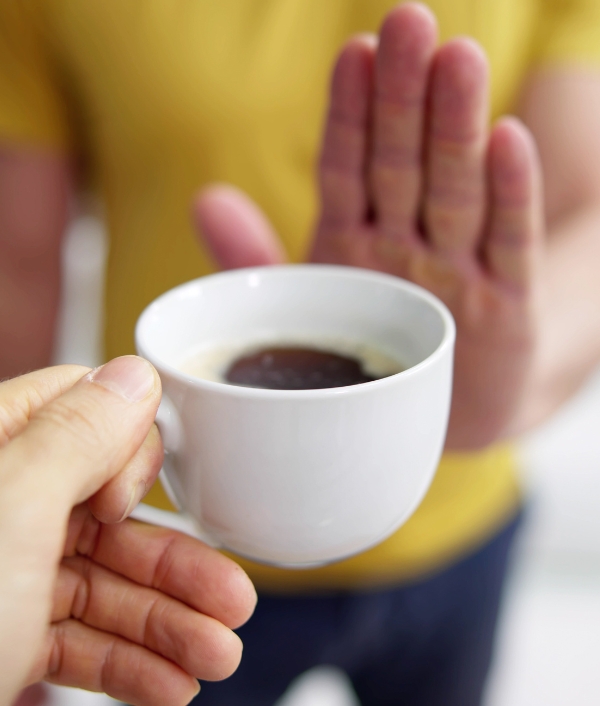 Eine Person bietet einer anderen Personen eine Tasse Kaffee an. Die andere Person verneint mit einem Handzeichen.