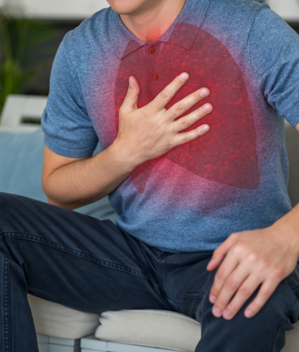 Das Bild zeigt einen Mann in dunkelblauer Hose und hellblauem T-Shirt, welcher sich auf die Brust greift weil er vermutlich eine Pneumonie hat.